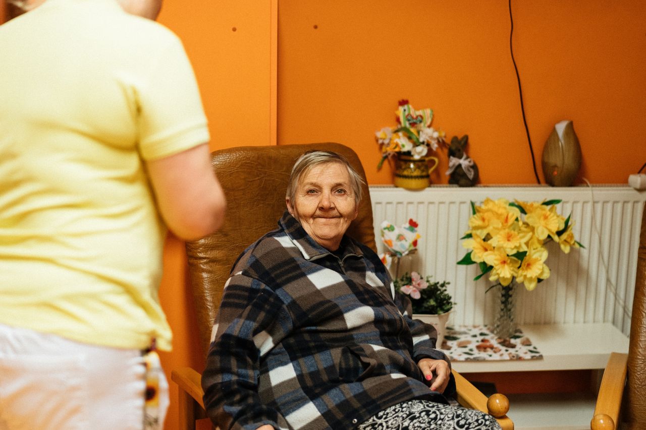 A caregiver attending to a content senior woman seated in her armchair at home