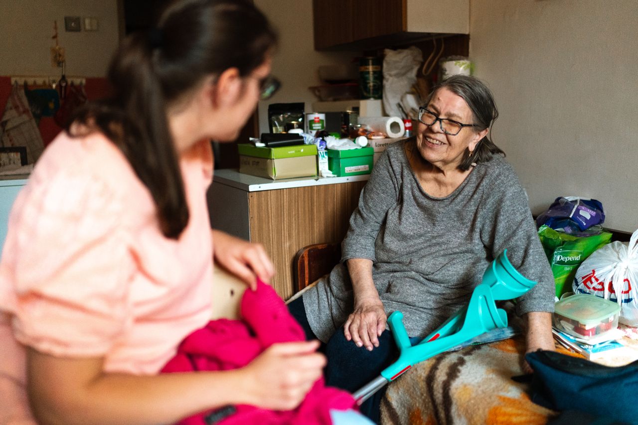 A caregiver helping a smiling senior woman steady herself with a walking crutch